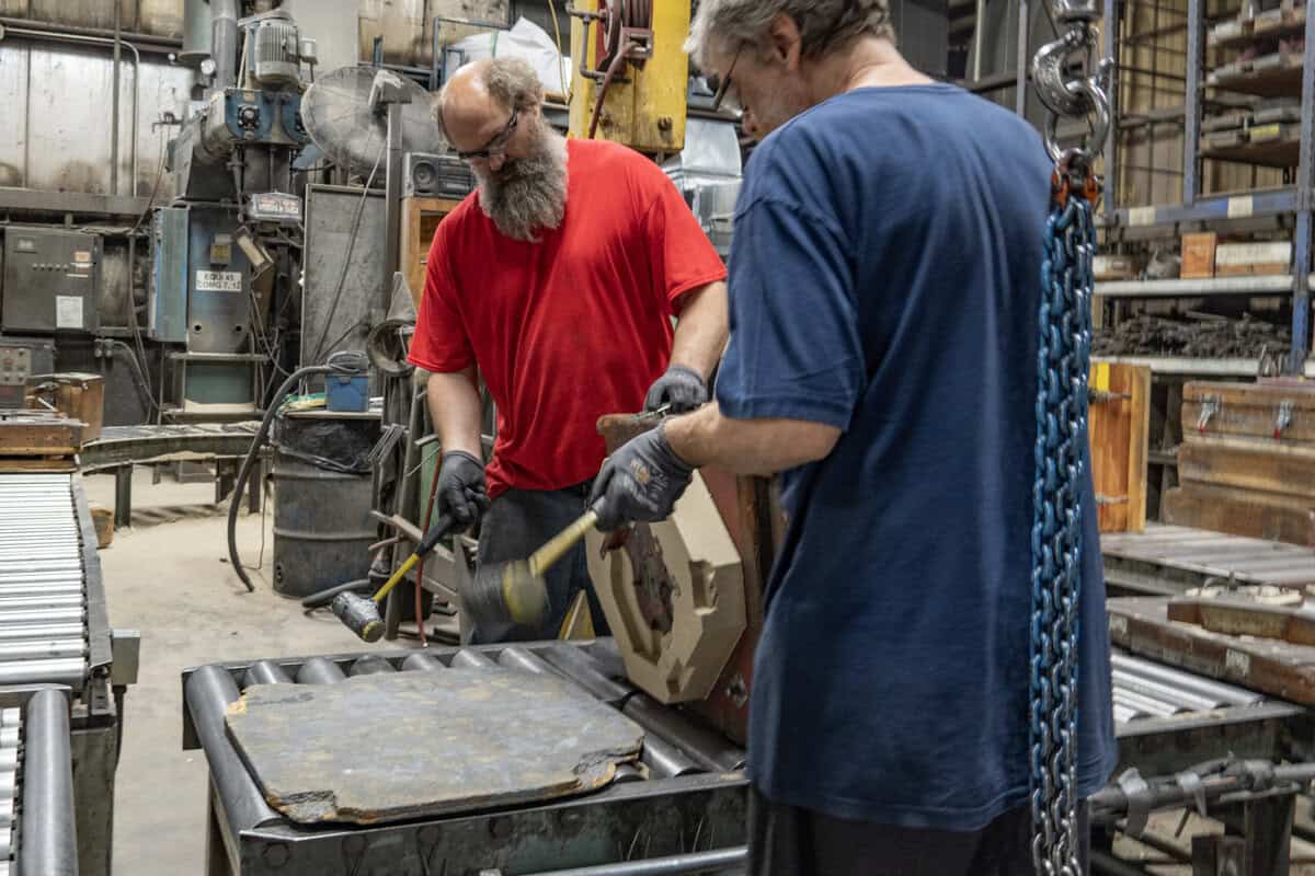 Two Men Working In Badger Foundry Hammering Something