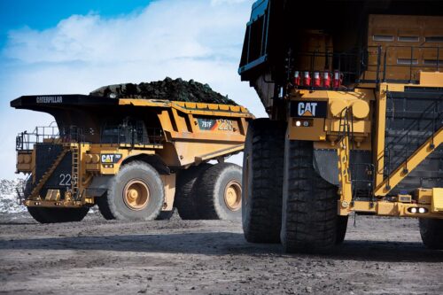 Two Very Large Dump Trucks On A Dirt Road.