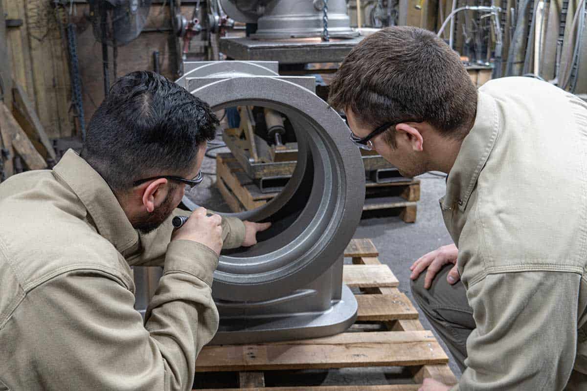 Two Badger Foundry Employees Inspecting An Iron Casted Part.